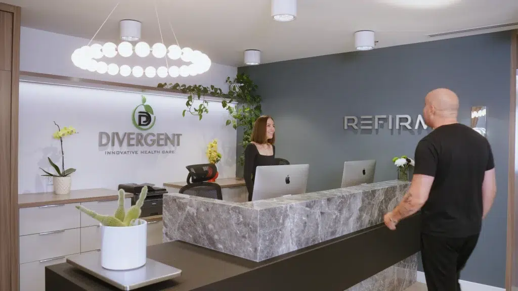 A receptionist at a health care clinic in Calgary welcomes a patient during a video production.