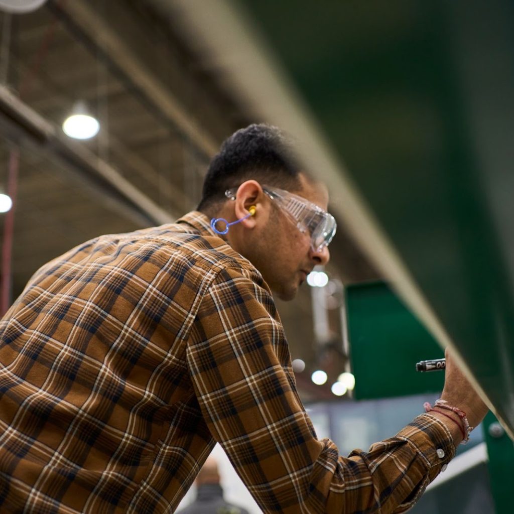 A person wearing safety glasses makes note of something with a marker during an internal comms video.