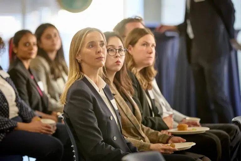 People at a conference pay attention to a speaker while being recorded in a video for professional services.