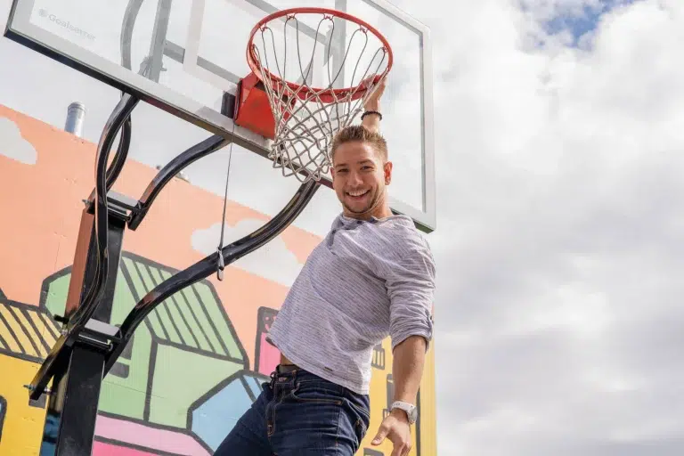 Someone smiles and hangs by one hand on a basketball hoop after a slam dunk in a b2b marketing video.