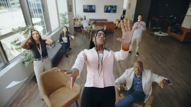 A person falls backwards into a room of coworkers during a creative video ad.
