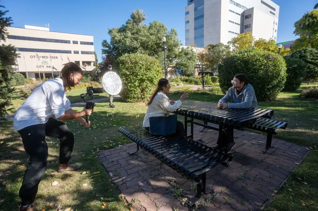 A videographer records two people at a picnic table at a video shoot on a sunny day in Calgary.