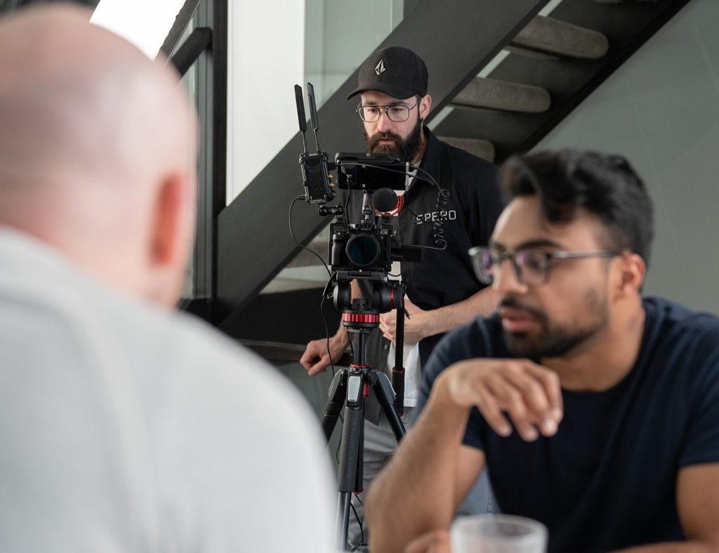 Videographer films two people talking with snack and beverages.